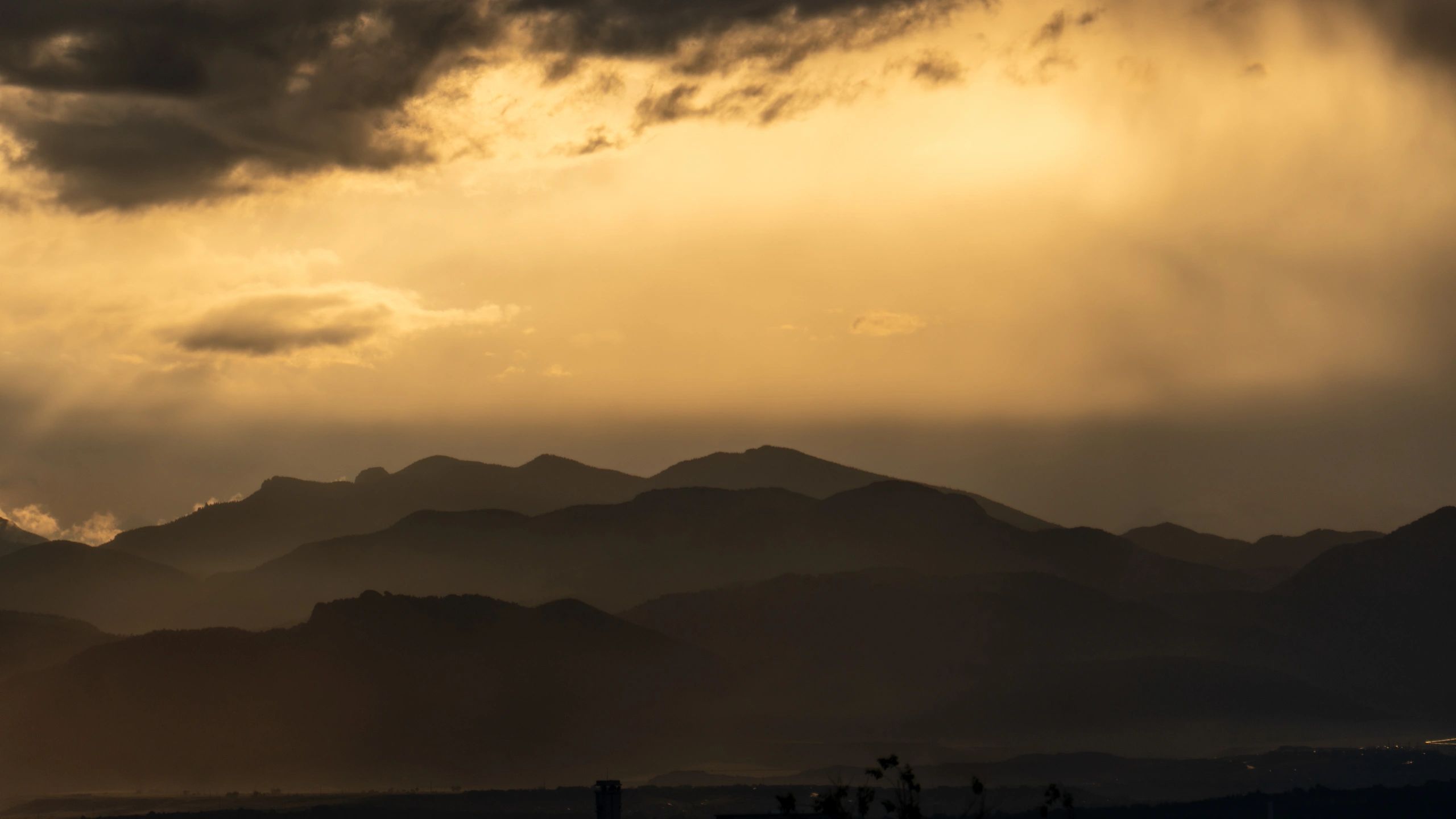 Sunset rays piercing storm clouds above layered mountain silhouettes